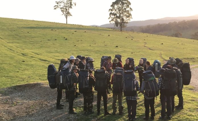 Big group of people gathered together wearing hiking backpacks outdoors